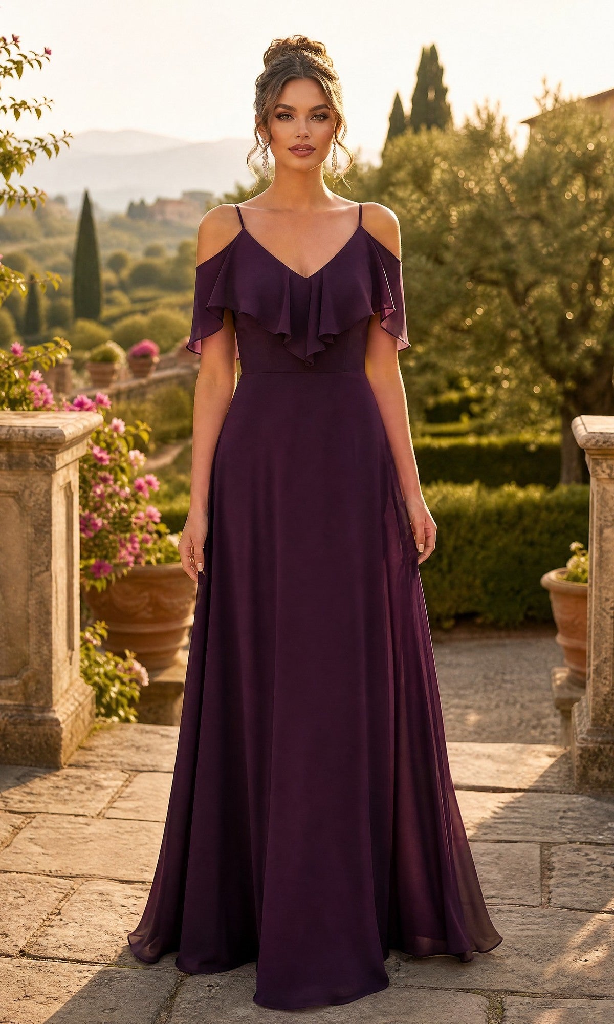 A woman stands outdoors amid greenery and stone architecture, wearing the Long Formal Dress: Chicas DM4004 in a plum hue, featuring a floor-length silhouette with cold shoulders, ruffle detailing, and delicate spaghetti straps.